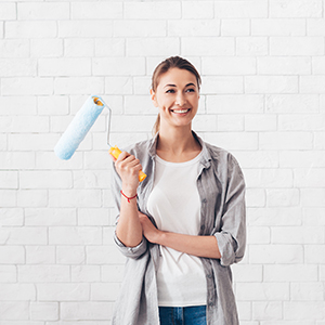 Repair concept. Young woman holding paint roller for renovation at home, happy expression, smiles at camera, white bricks wall, panorama, copy space